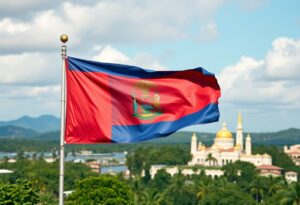 A red and blue flag with a central emblem featuring a symbol flies against a backdrop of trees, distant hills, and a building with golden domes under a cloudy sky.