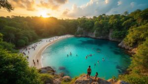 People swim and relax along a crescent-shaped beach with turquoise water, surrounded by dense forest and cliffs, as the sun sets. A Belize travel guide could help you explore hidden spots like this, where two people stand on a rocky outcrop overlooking the scene.