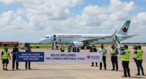 Airport staff and officials hold a banner reading “Belize Welcomes Air Canada Montreal Flight” in front of an Air Canada airplane on the tarmac under a partly cloudy sky, celebrating the new Belize flight connecting to Air Canada Montreal.