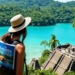 A woman in a hat and backpack stands overlooking turquoise water and dense green forest, with a stone temple below—discovering the hidden gems of Belize San Pedro. Her backpack holds "The Xamanek Belize," its cover adorned with a shell.