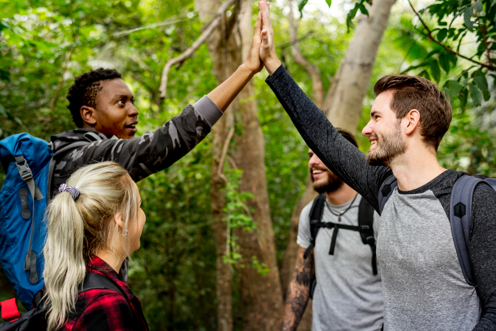 Two men high-fiving with a group of friends during a hike in the woods, feeling as joyful and united as if they were at home.
