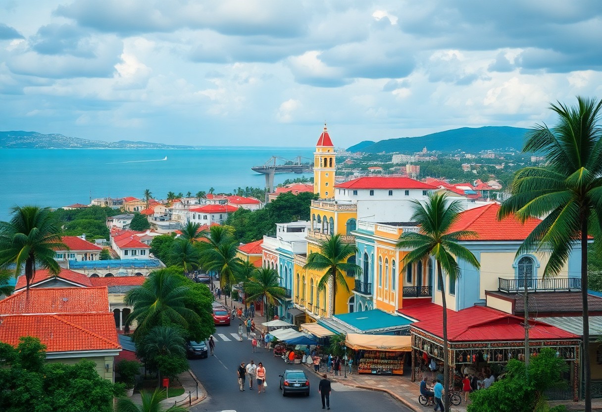 A vibrant seaside town with colorful buildings, palm trees, and a busy street lined with people and cars. A tall yellow clock tower stands prominently in the center. The blue ocean is visible in the background under a cloudy sky.