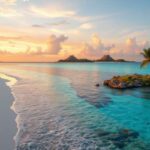 A sandy beach with clear turquoise water at sunset, palm trees along the shore, and a small rocky island in the water—Placencia Beach is the perfect Belize travel destination under a partly cloudy sky with distant mountains.